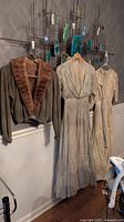 Photo showing two Victorian dresses and one cashmere sweater hanging on a wall-mounted rack.