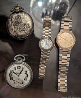 Overview of two pocket watches (top left and bottom left) and two wristwatches (right) on glass surface