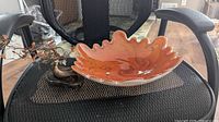Orange and gold swirled Venetian glass bowl with ruffled edge on black mesh chair.