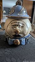 Front view of vintage handmade ceramic clown cookie jar depicting facial details and blue hat and bow tie
