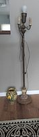 Full view of a tall antique floor lamp next to a colorful Majolica style ceramic vase on the floor.
