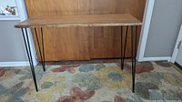 Front view of mcm style desk or sofa table with wood top and thin black metal legs.
