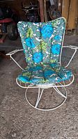 Front view of the patio chair with floral cushion, showing swivel wireframe base and armrests.