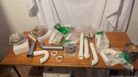 Full lot view showing multiple new plumbing parts including PVC pipes, elbows, fittings, and flexible hoses on a wooden table.