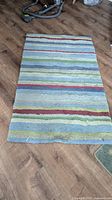 Top view of rectangular area rug with multicolored horizontal stripes on a wood floor.
