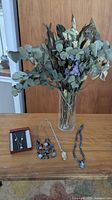 Overview of lot showing dried flowers in vase, boxed necklace and earrings set, and three pieces of beaded jewelry on wooden surface.