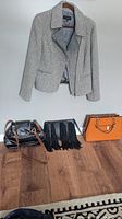 Talbot gray zippered jacket on hanger with three handbags on floor: black handbag with brown trim, black fringe handbag, and an orange handbag