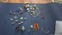 Full lot overview showing assorted vintage costume jewelry, sunglasses, jewelry pliers on dark blue textured background.