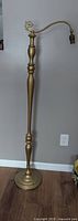 Full view of antique floor lamp against a wall showing its height and gold gilt finish along with the metal top attachment and base.