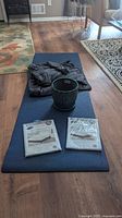 Yoga mat laid out on floor with weighted blanket folded on it, teal pot, and two packaged queen size mattress protectors on yoga mat.