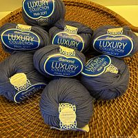 Eight balls of Diamond Luxury Pima Soft yarn displayed on wicker surface