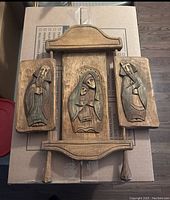 Front view showing the three carved wood panels with religious figures mounted on a decorative wood plaque.