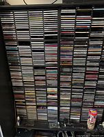 Front view of black shelving unit filled with rows of music CDs in jewel cases, arranged vertically and horizontally.