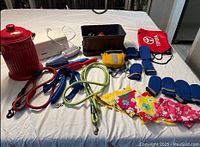 Photo showing all dog supplies laid out on a white surface including leashes, dog boots, bandanas, grooming brushes, dog waste bin, and toy container