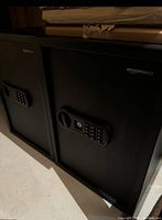 Two matte black AmazonBasics electronic safes side by side, showing keypad and handle on front.
