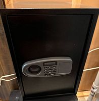 Large black electronic safe showing closed front with digital numeric keypad and recessed handle.