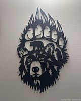 Black metal wall art shaped like a bear's head with a bear paw outline forming a flame design