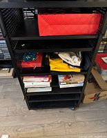Front view of black metal music equipment cart filled with various music-related items including boxes and papers.
