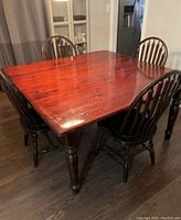 Solid wood square dining table with reddish-brown finish and four matching spindle-back chairs arranged around it.