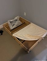 Photo showing rectangular wicker under bed storage basket with cloth cover partially unzipped, containing a clear plastic bag filled with white plastic clothes hangers.