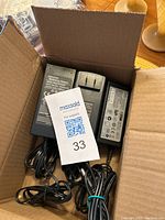Three black 12 Volt power supply adapters in a cardboard box with attached cords and plugs
