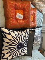 Two burnt orange reversible velvet and damask pillows placed behind two navy and white floral patterned indoor/outdoor pillows on a bed surface