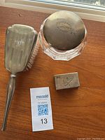 Photo of the sterling hairbrush with bristles, crystal powder bowl with sterling lid, and sterling match cover with letter H engravings on wood surface.
