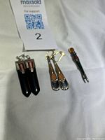 Photo showing two pairs of earrings: one black jet drop pair with red and white diamond shaped details, one brown and black enamel drop pair with clear stones at the bottom. Also shows Scottish silver pin with citrine and bloodstone.