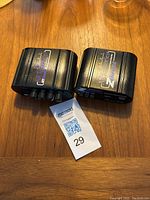 Two black audio devices on wooden surface, one labeled My Monitor 2, the other ZDirect, with a MaxSold tag number 29