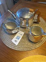 Vintage British Picquet Ware tea set including teapot, creamer, and sugar bowl displayed on a woven placemat on a wooden table, showing wear on handle.