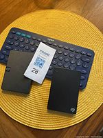 Two Seagate external hard drives and one Logitech Bluetooth keyboard placed on a woven round placemat.
