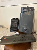 Grey Kyvol humidifier, small black ceramic heater, and black power bar with six outlets on carpeted floor