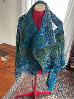 Shawl draped over mannequin from front showing textured blue and green mixed textile with loop patterns.