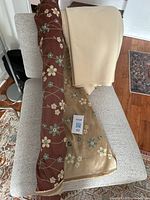 Fabric roll showing brown and gold sides with floral embroidery and beige heavy cotton/linen blend fabric folded beside it.