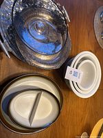 Photo showing a large silver-tone metal serving platter with handles, stack of three white ceramic Corelle bowls and a divided serving dish with two sections.