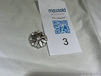 Clear rhinestone brooch placed on a white fabric background showing the front design and detailing, with auction tag.