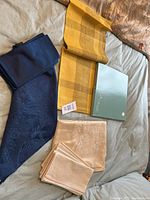 Photo of folded blue damask and cream damask napkins with yellow plaid runner and box, set on bed