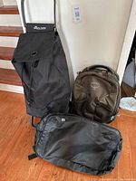 Black Rolser rolling bag with handle, green Osprey backpack, and MEC large gym bag on wooden floor.