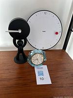 Lot of three clocks arranged on a wooden surface: the MoMA clock, the Umbra person clock, and the aqua glass Phinney-Walker clock in front.