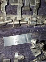 Close-up photo of metal tag marked B1159585 1904 and several sewing machine attachments secured in case.