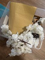 Plastic container with artificial white flower stems and yellow corrugated cardboard sheet