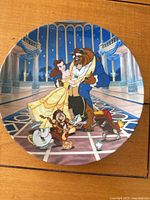 Front of round collectors plate depicting Belle and Beast dancing in castle ballroom with other characters.