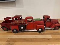 Shows three red tin vintage-style trucks, side by side, highlighting their size and design differences.