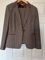Front view of brown plaid blazer on hanger showing single button and suede-like collar detail.