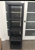 Front view of black shelving unit with five shelves against door background.