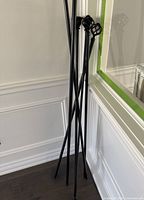 Photo of six black metal curtain rods with cage-style decorative finials leaning against a wall near a mirror and white wainscoting.