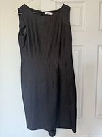 Grey sleeveless fitted dress hanging against a white door, showing its simple and elegant shape with stitching detail