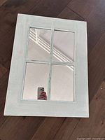 Wood framed windowpane mirror with four glass panes in distressed white finish on wooden floor.