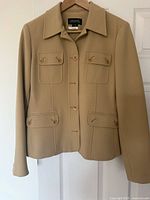 Beige blazer with collar, four buttoned flap pockets on front, button-up closure on hanger