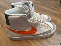 Side view of Nike Blaze high top sneakers showing white leather upper with orange swoosh and black heel tab.